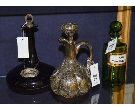 A white metal clad clarinet jug, decorated with grapes and vine leaves, including a blue glass decanter and green apothecary 