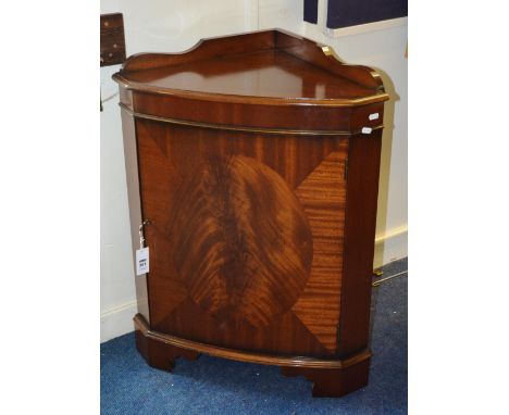 A George III style mahogany corner cabinet, with shaped back panel, moulded top and oval veneered door, raised on bracket fee