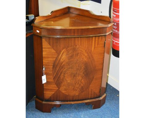 A George III style mahogany corner cabinet, with shaped back panel, moulded top and oval veneered door, raised on bracket fee