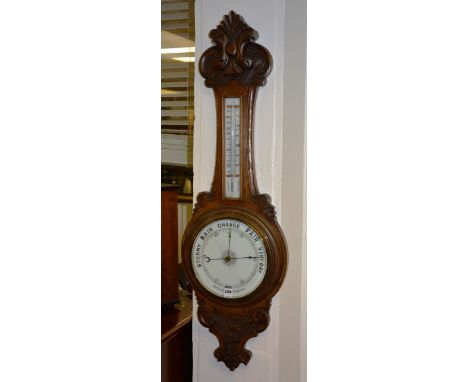 An oak cased aneroid barometer, with scroll carved pediment over trunk thermometer and white dial, 90cm high