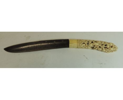 A 19th Century Indonesian dagger with ornately carved ivory hilt worked with demons and figures and with original old curved 