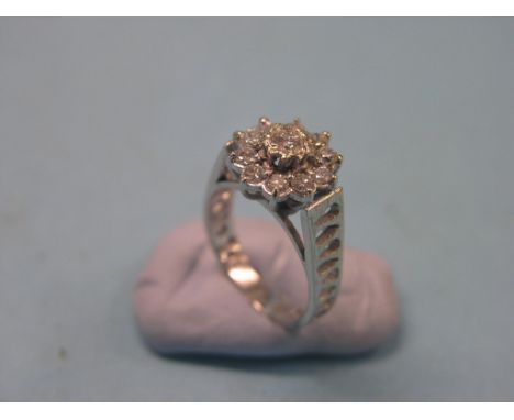 A diamond cluster ring, rosette design of eleven stones, pierced white metal shank, size M/N 