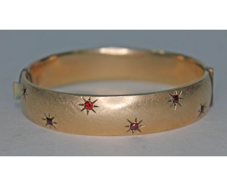A yellow metal bangle set with red paste. 