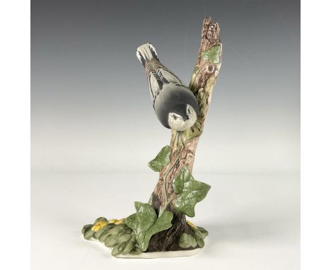 A hand painted bisque porcelain figure of a grey and brown bird perched on a tall tree branch adorned with leaves. Boehm back