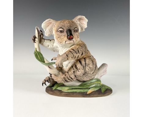 A hand painted bisque porcelain sculpture of a brown koala bear sitting on a branch and holding a leaf. Boehm backstamp. Issu