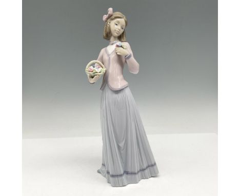 A young woman in a pink sweater and long lavender skirt holding a basket of flowers while admiring a few from the set. Lladro