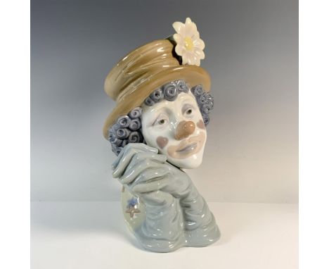 A glossy figural bust of a clown with a sad expression, holding their hands. Lladro backstamp. This item has its original box