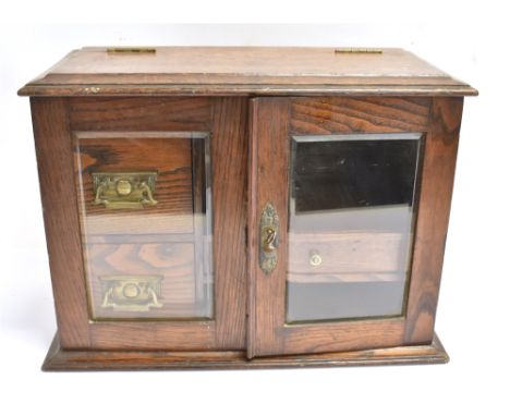 AN OAK SMOKERS CABINET  with hinged top and glazed doors opening to interior fitted with drawers and pipe rack, with carrying