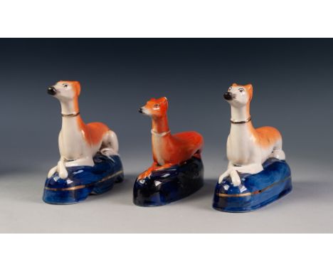 PAIR OF 19th CENTURY STAFFORDSHIRE POTTERY MODELS OF RECUMBENT GREYHOUNDS, on dark blue glazed pedestal bases as pen stands, 