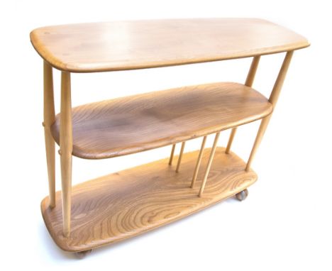 An Ercol light elm Windsor low bookshelf trolley, three tiers supported on shaped legs and dowel dividers to the lower shelf,