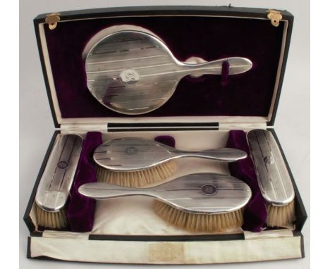 A cased hallmarked silver dressing table set, comprising a hand mirror and two pairs of brushes, all with engine turned decor