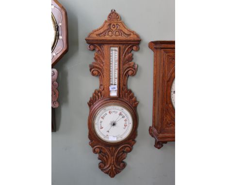 A late 19th Century oak cased aneroid barometer, the carved foliate case set with a twin scale porcelain thermometer (as foun