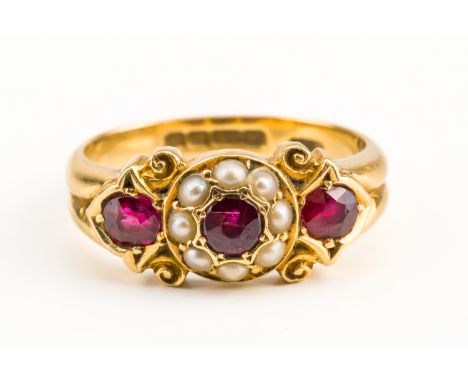 AN 18CT GOLD, RUBY AND HALF PEARL RINGMounted with three cushion shaped rubies and with eight half pearls to the central clus