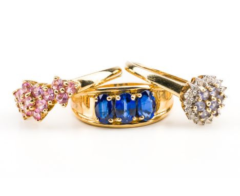 A 9CT GOLD AND SAPPHIRE THREE STONE RING AND TWO FURTHER RINGS (3)The first ring claw set with a row of three oval cut sapphi