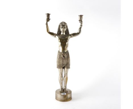 A 20TH CENTURY SILVERED METAL FIGURAL CANDLESTICK OF EGYPTIAN DESIGNStanding holding two candle sconces, 60cm high