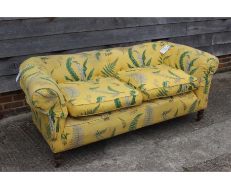 An early 20th century Chesterfield settee, upholstered in a leaf printed yellow linen, on turned and castored supports, 72" w