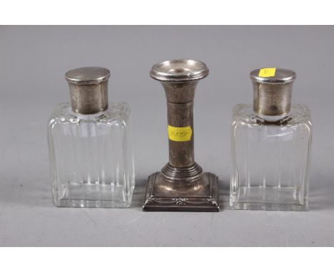 A pair of cut glass and silver topped scent bottles and stoppers, 4 1/4" high, and a filled silver candlestick, on square bas
