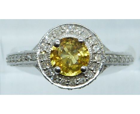 An 18k white gold ring set with a round cut yellow sapphire surrounded by diamonds with further diamonds to the setting and m