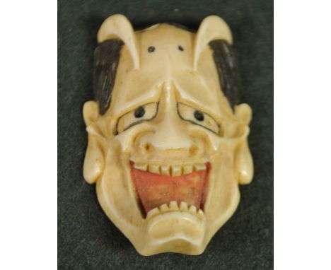 A Japanese ivory netsuke, carved as a grotesque noh mask, painted features, 4.5cm long, signed, Meiji period