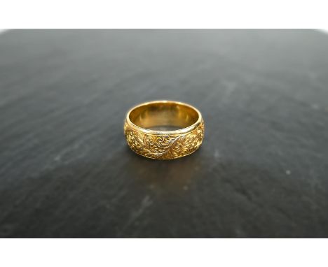 An 18 ct hallmarked gold wedding ring with extensive chased decoration, 8.8 gms, size 'O'-'P'.In good condition.WE TAKE GREAT