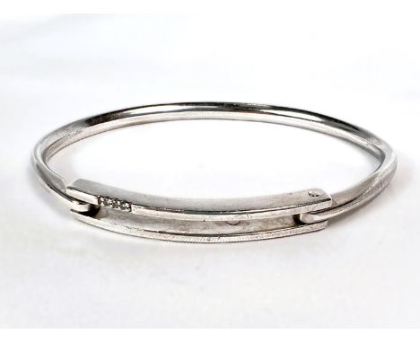 A white metal bangle with hinged opening, the top set with four small diamonds (one chipped), stamped 925, 23.5gm.