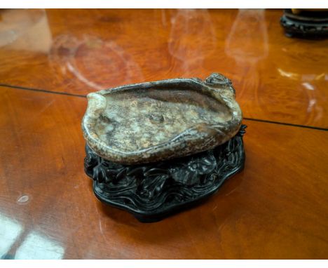 A Chinese carved jade coloured hardstone in the form of a monkey on edge looking into pool on fitted hardwood stand with pier
