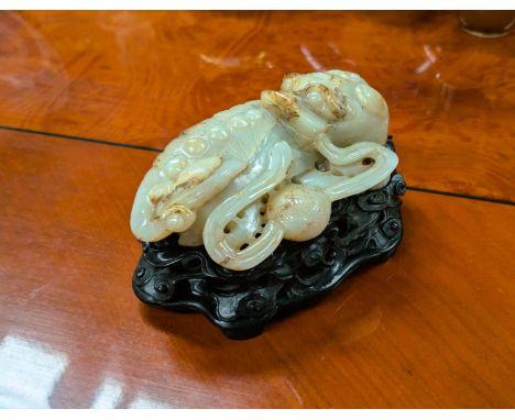 A Chinese carved mutton fat jade lion, curled, with ebonised pierced stand with cloud decoration, lion length 15.5cm.Conditio