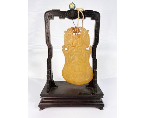 A Chinese yellow jade coloured panel hanging from hardwood stand, geometric decoration, panel 15cm, overall height 23cm.