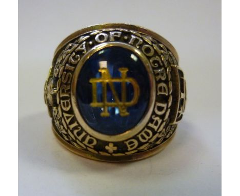 A gold coloured metal signet style ring, cast around a blue stone (engraved ND) with the inscription 'Aniversity op Notre Dam