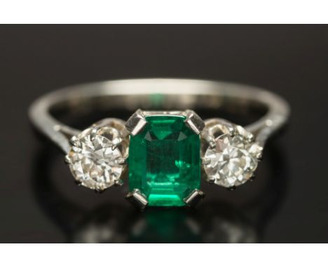 An emerald and diamond three-stone ring: with central emerald-cut emerald approximately 0.7ct between round old brilliant-cut