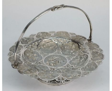 A Burmese silver swing handle pedestal dish: of circular form, with circular embossed panels depicting village scenes, within