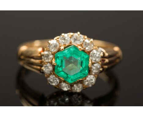 A gold, emerald and diamond circular cluster ring: with central hexagonal emerald, approximately 0.75cts, claw-set within a s