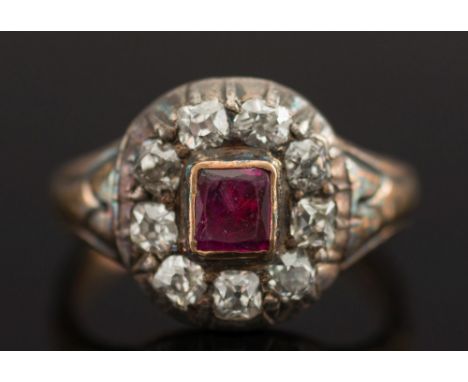 A ruby and diamond oval cluster ring:, with central, rectangular ruby in rub-over setting, within a surround of old-cut diamo
