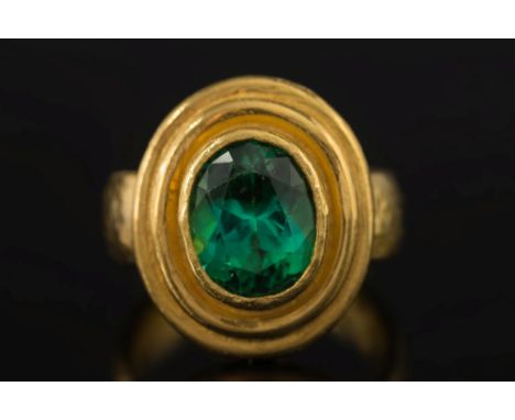 A 22ct gold and oval green tourmaline single-stone ring by Charmian Harris:, the shank and bezel of hammered finish, the gree