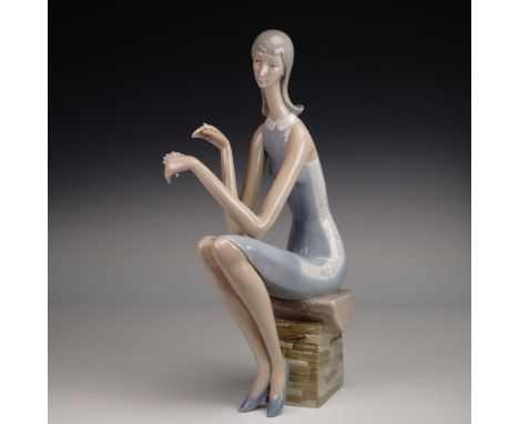 Elegant and elongated in form, this Lladro porcelain figurine titled He Loves Me (No. 4599) depicts a young woman seated grac
