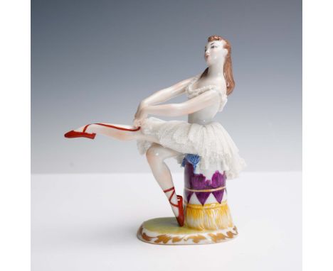 This finely modeled Lladro porcelain figurine depicts a young ballerina seated atop a tasseled cushion as she adjusts her red