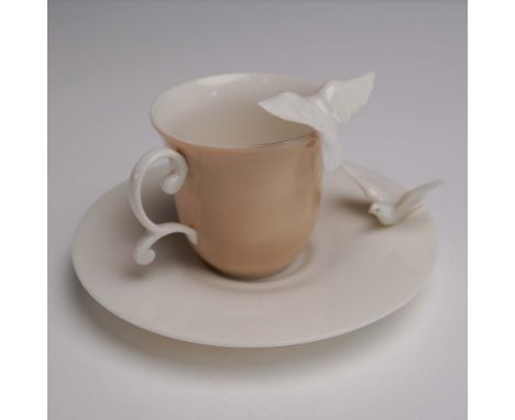 Elegant porcelain cup and saucer set features a soft peach colored cup and a creamy white saucer, enhanced by delicate white 
