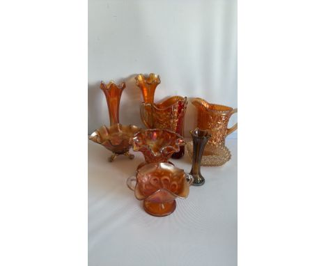 Collection of seven carnival glass items, including bowls, vases, and a pitcher in vibrant orange and red hues with intricate