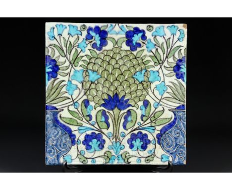 A large William de Morgan earthenware tile in Iznik style, the central floral motif flanked by urns, painted in underglaze to