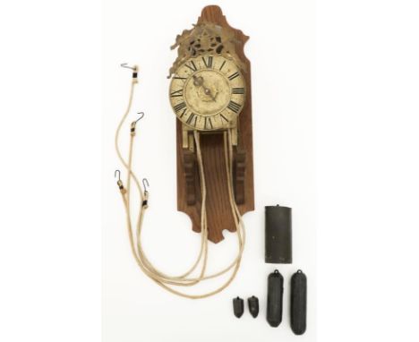 Brass and on a wood support, the dial face with Roman numerals and crowned with an openworked decorative panel. The mechanism