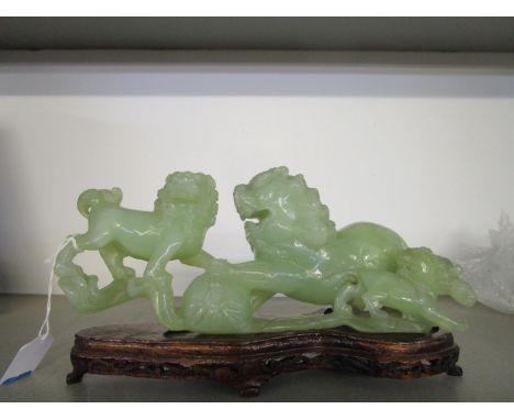 A Chinese green jade carved group of three lion dogs 10 7/8" long, mounted on a wooden base 