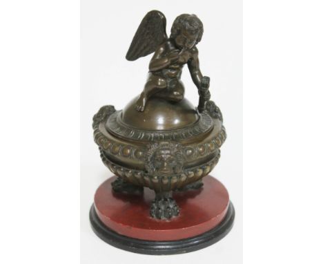 A bronze inkwell formed as a cherub sat on a domed lid above the gadrooned base with lion masks and claw feet sat on round pl