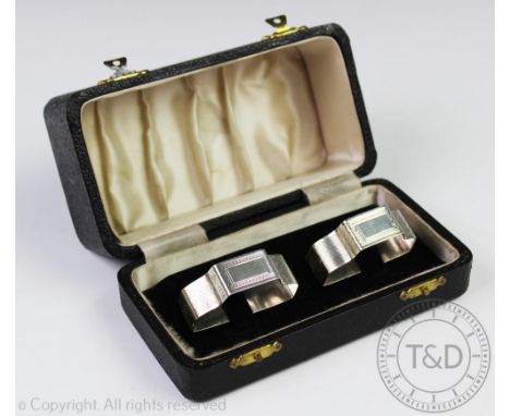 A cased pair of silver Art Deco napkin rings, E Silver & Co, London 1945, of angular shape with engine turned exterior bearin