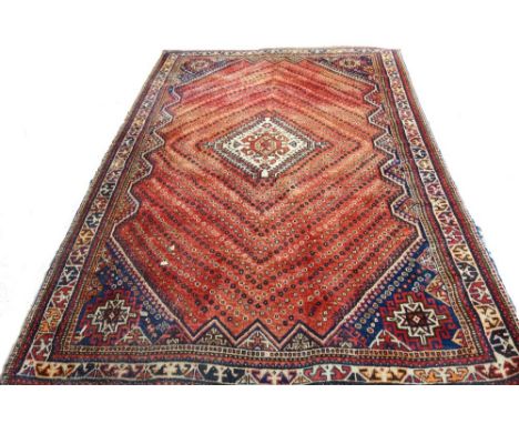 A Shiraz rug, South Persian, the madder field with an indigo hooked medallion surrounded by diagonal bands of mini flowerhead