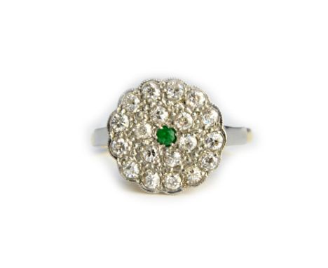 A gold and platinum, emerald and diamond set shaped circular cluster ring, mounted with the circular cut emerald at the centr