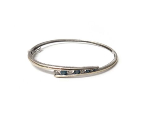 A white gold, diamond and treated blue diamond set oval hinged bangle, the front mounted with a row of alternating circular c