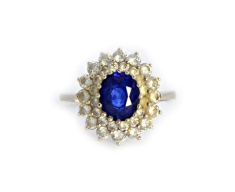 A white gold, sapphire and diamond set oval cluster ring, claw set with the oval cut sapphire at the centre, within a two row