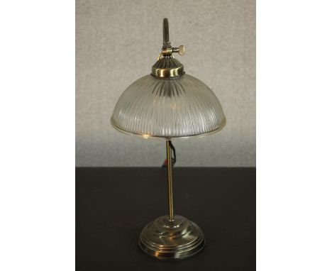 An early 20th century style brass desk lamp, with a holophane style glass shade, adjustable stem and circular base. H.53cm. 