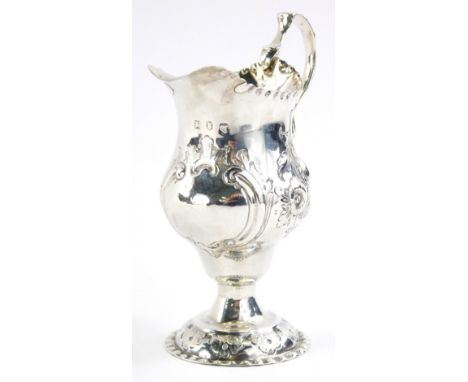 A George III silver cream jug, the helmet shaped body with ear handle repousse decorated with scrolls and flowers, on an inve