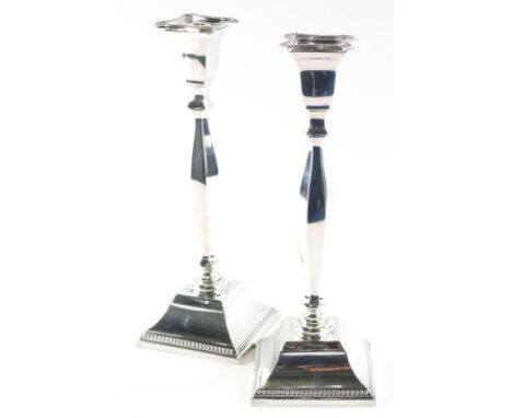 A pair of Elizabeth II silver candlesticks, each with inverted square dish holders on turned stems and square bases with a be